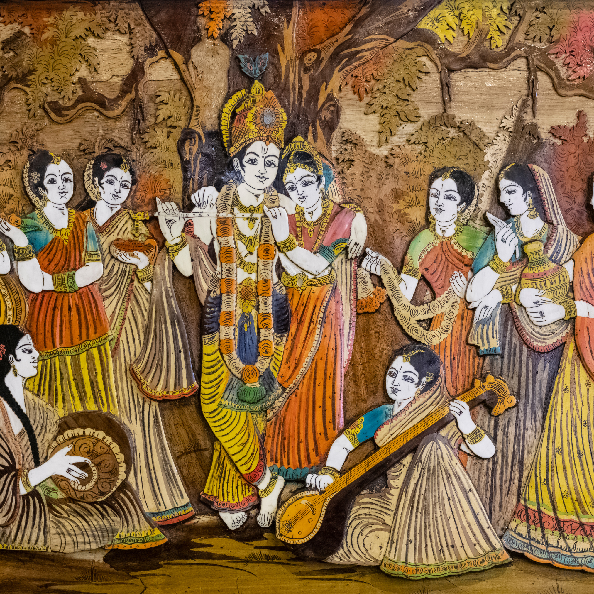 A traditional Indian art piece, possibly a wood inlay, depicting Krishna playing the flute while surrounded by Radha and gopis in a forest setting. 
